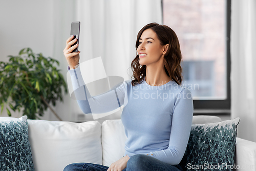 Image of happy woman with smartphone taking selfie at home