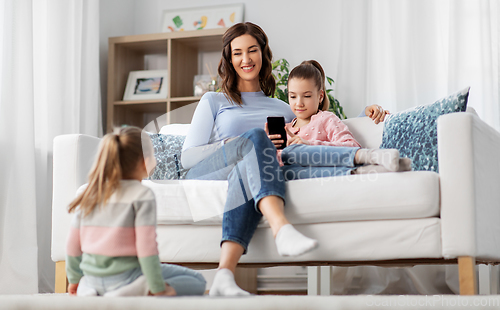 Image of happy mother and daughters with smartphone at home