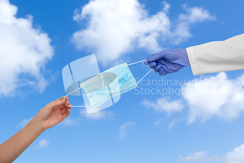 Image of hand of doctor giving mask to patient over sky