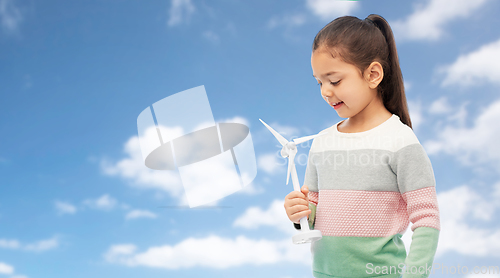 Image of smiling girl with toy wind turbine over blue sky