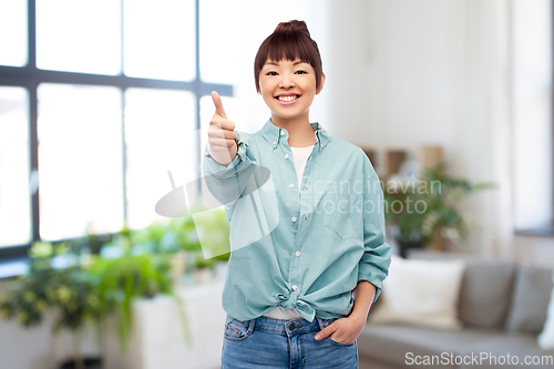 Image of happy asian woman showing thumbs up over home