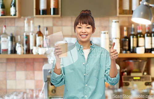 Image of asian woman with coffee showing thumbs up at bar