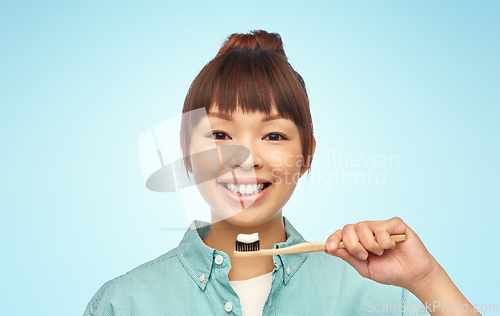 Image of asian woman with toothpaste on wooden toothbrush