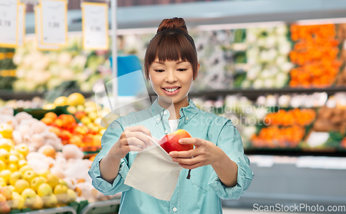 Image of happy woman putting apple into reusable bag