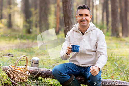 Image of man with basket of mushrooms drinks tea in forest