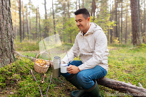 Image of man with basket of mushrooms drinks tea in forest