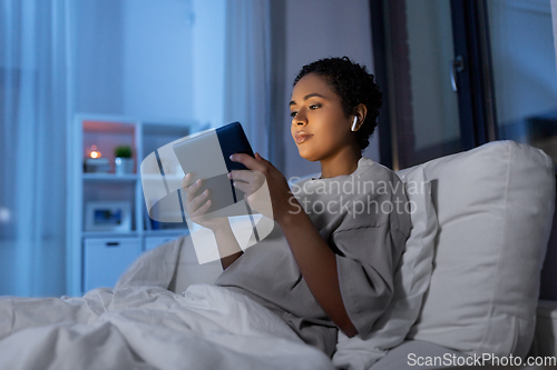 Image of woman with tablet pc in earphones in bed at night