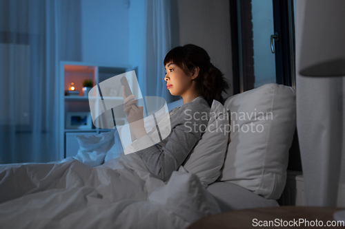 Image of asian woman with smartphone in bed at night