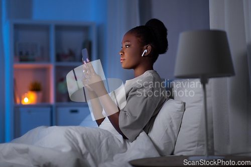 Image of woman with smartphone and earbuds in bed at night