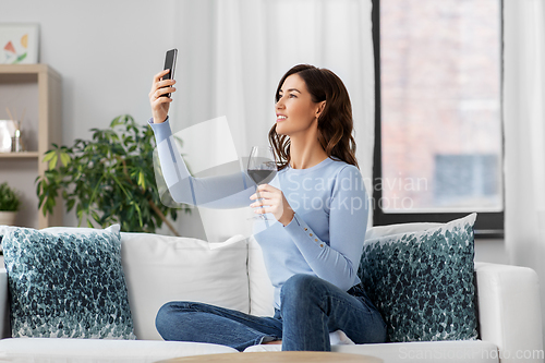 Image of woman with smartphone and wine taking selfie