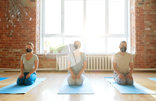 Image of group of people in masks meditating at yoga studio