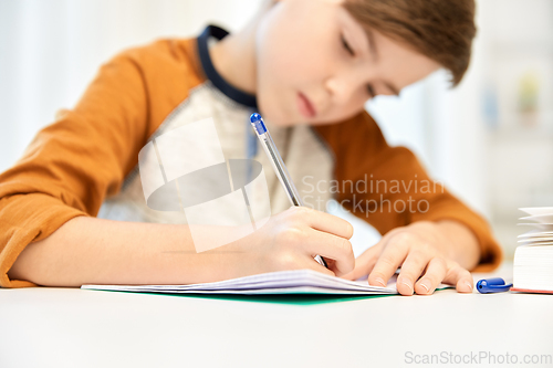 Image of student boy with book writing to notebook at home