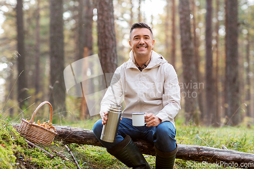 Image of man with basket of mushrooms drinks tea in forest