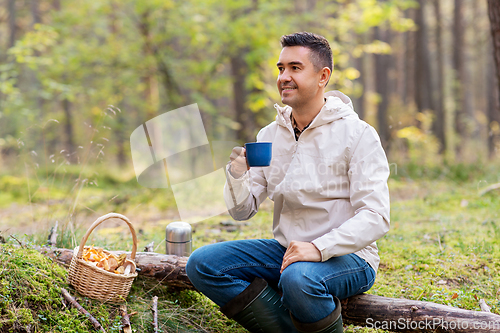 Image of man with basket of mushrooms drinks tea in forest