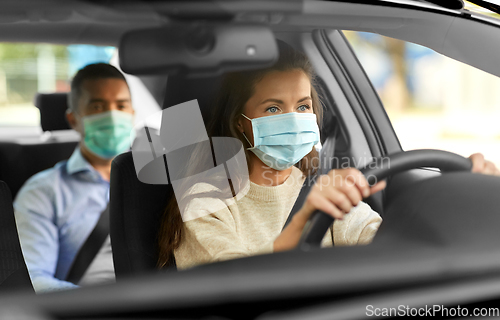 Image of female driver in mask driving car with passenger