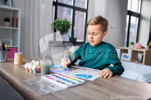 Image of boy with colors and brush drawing picture at home