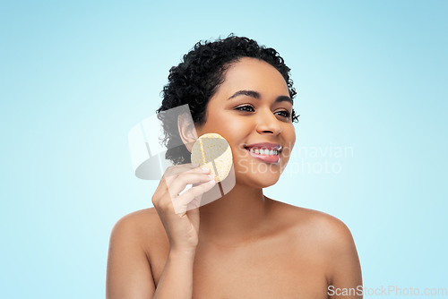 Image of young woman cleaning face with exfoliating sponge