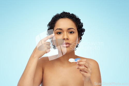 Image of african american woman putting on contact lenses