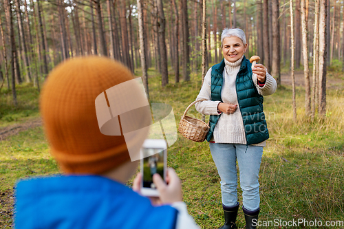 Image of grandson photographing grandmother with mushroom