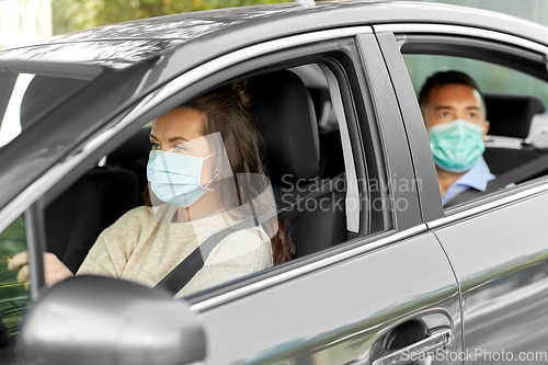 Image of female driver in mask driving car with passenger