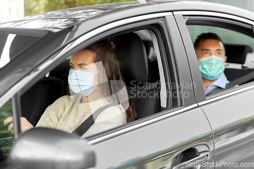 Image of female driver in mask driving car with passenger