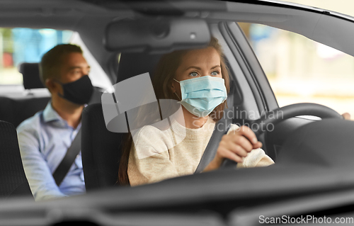 Image of female driver in mask driving car with passenger