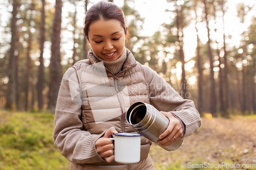 Image of asian woman with thermos drinking tea in forest