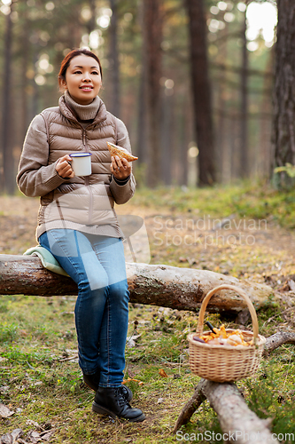 Image of woman with mushrooms drinks tea and eats in forest