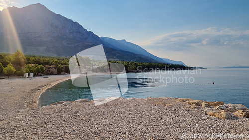 Image of Beautiful shore of the Adriatic Sea. Sunrise with rays of sun over Biokovo Mountain Nature park and trees from Makarska Riviera-Biokovo, Dalmatia, Croatia, Europe