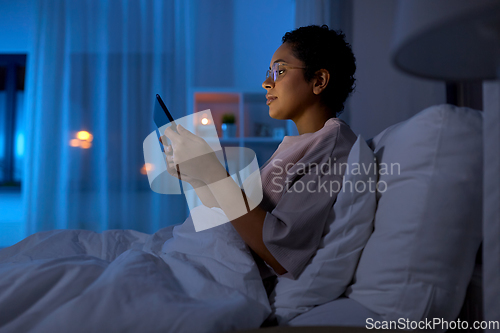 Image of woman with tablet pc in bed at home at night