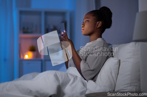 Image of woman with smartphone in bed at home at night