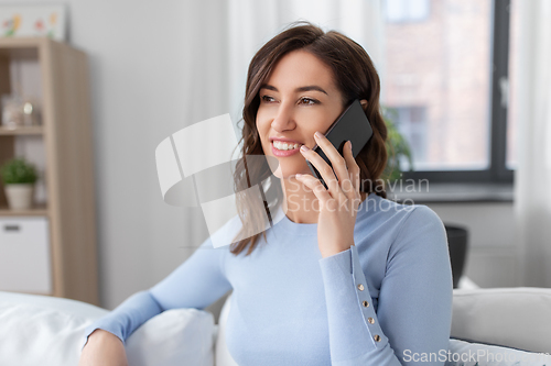 Image of smiling woman calling on smartphone at home