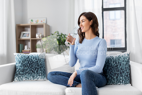 Image of woman drinking water from glass bottle at home