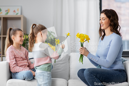 Image of daughters giving daffodil flowers to happy mother