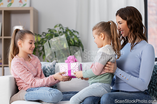 Image of girl giving present to younger sister at home