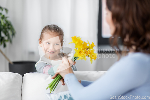 Image of happy daughter giving daffodil flowers to mother