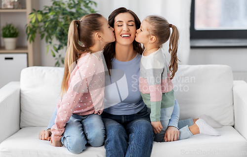 Image of happy mother and two daughters kissing her at home