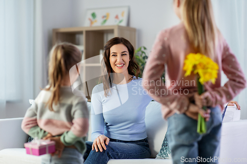Image of daughters giving flowers and gift to happy mother
