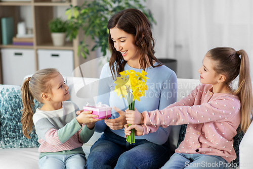 Image of daughters giving flowers and gift to happy mother