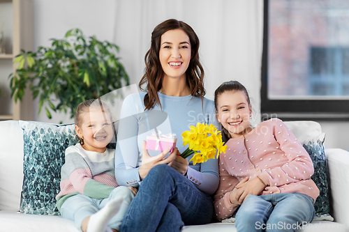 Image of daughters giving flowers and gift to happy mother