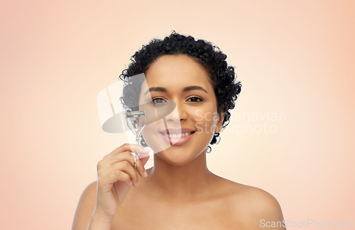 Image of smiling african american woman with eyelash curler