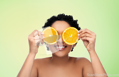 Image of smiling african woman making eye mask of oranges