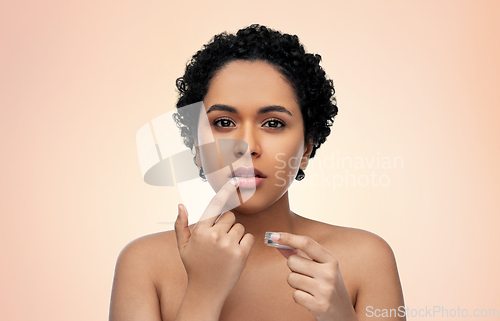 Image of african american woman applying lip gloss