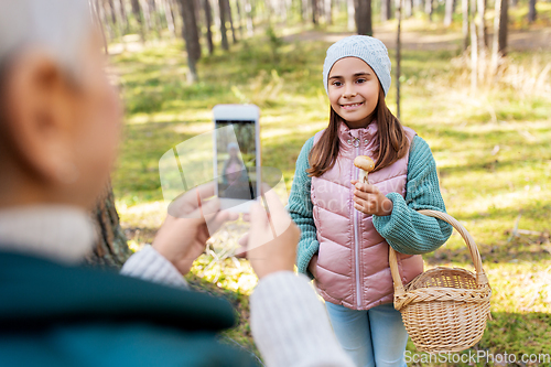 Image of grandma photographing granddaughter with mushrooms