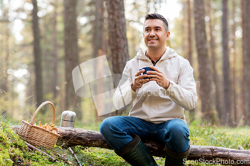 Image of man with basket of mushrooms drinks tea in forest