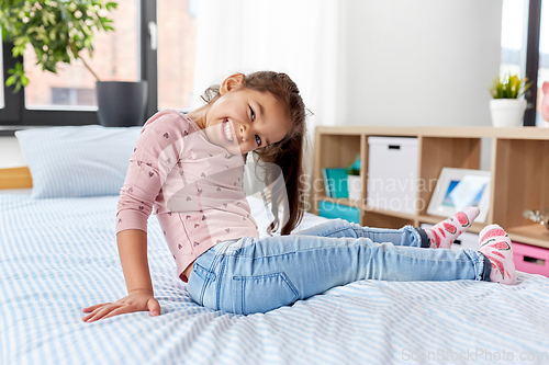 Image of happy smiling little girl sitting on bed at home