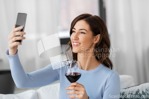 Image of woman with smartphone and wine taking selfie