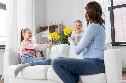 Image of daughters giving daffodil flowers to happy mother