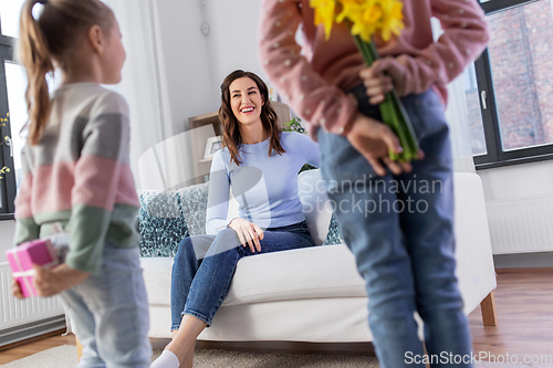 Image of daughters giving flowers and gift to happy mother