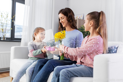 Image of daughters giving flowers and gift to happy mother